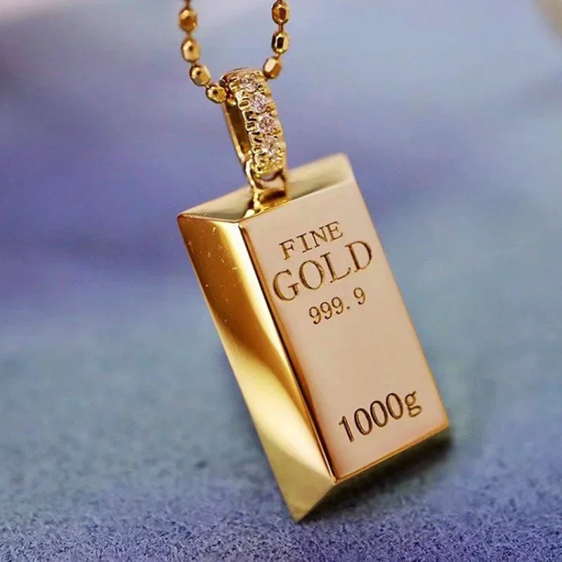 Gold pendant shaped like a gold bar with 'FINE GOLD 999.9 1000g' text on a blurred background