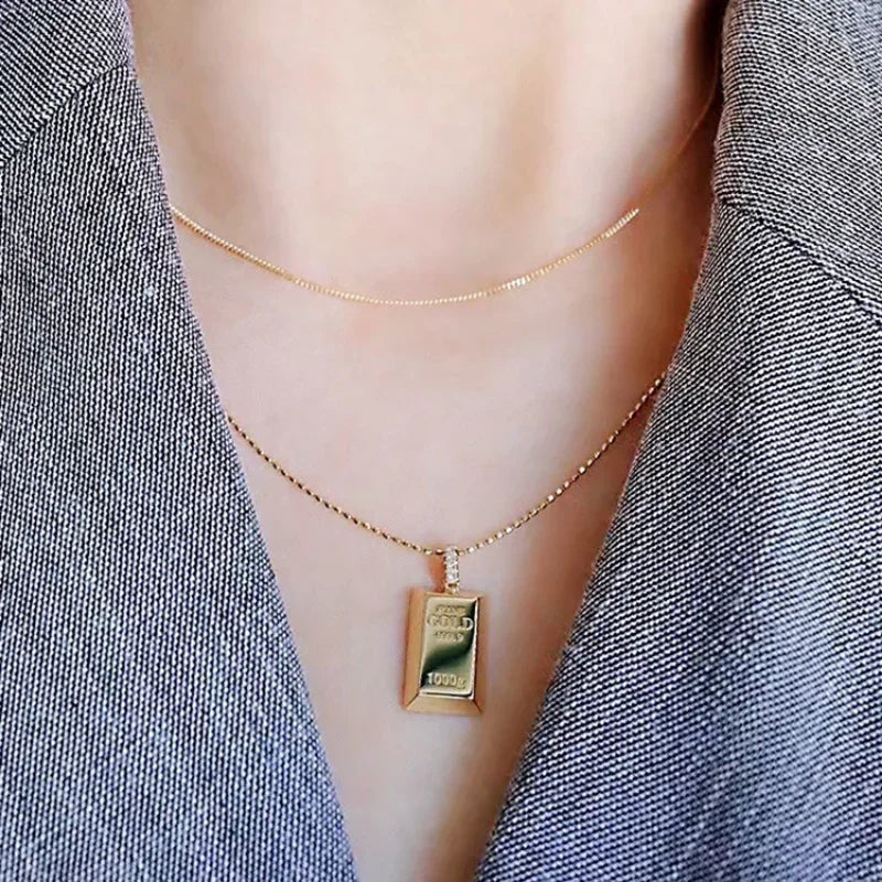 Gold necklace with a gold bar pendant on a person wearing a gray blazer.