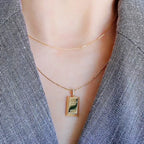 Gold necklace with a gold bar pendant on a person wearing a gray blazer.
